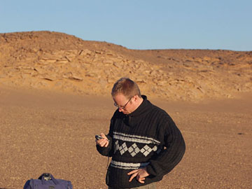 Libya: Dr Sebastian Frohlich takes a GPS reading on the border of the Sahara desert in Southern Libya, near to Sabah.