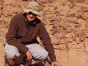 Libya: Dr Stefan Bodin next to a piece of silicified wood, Messak Formation.